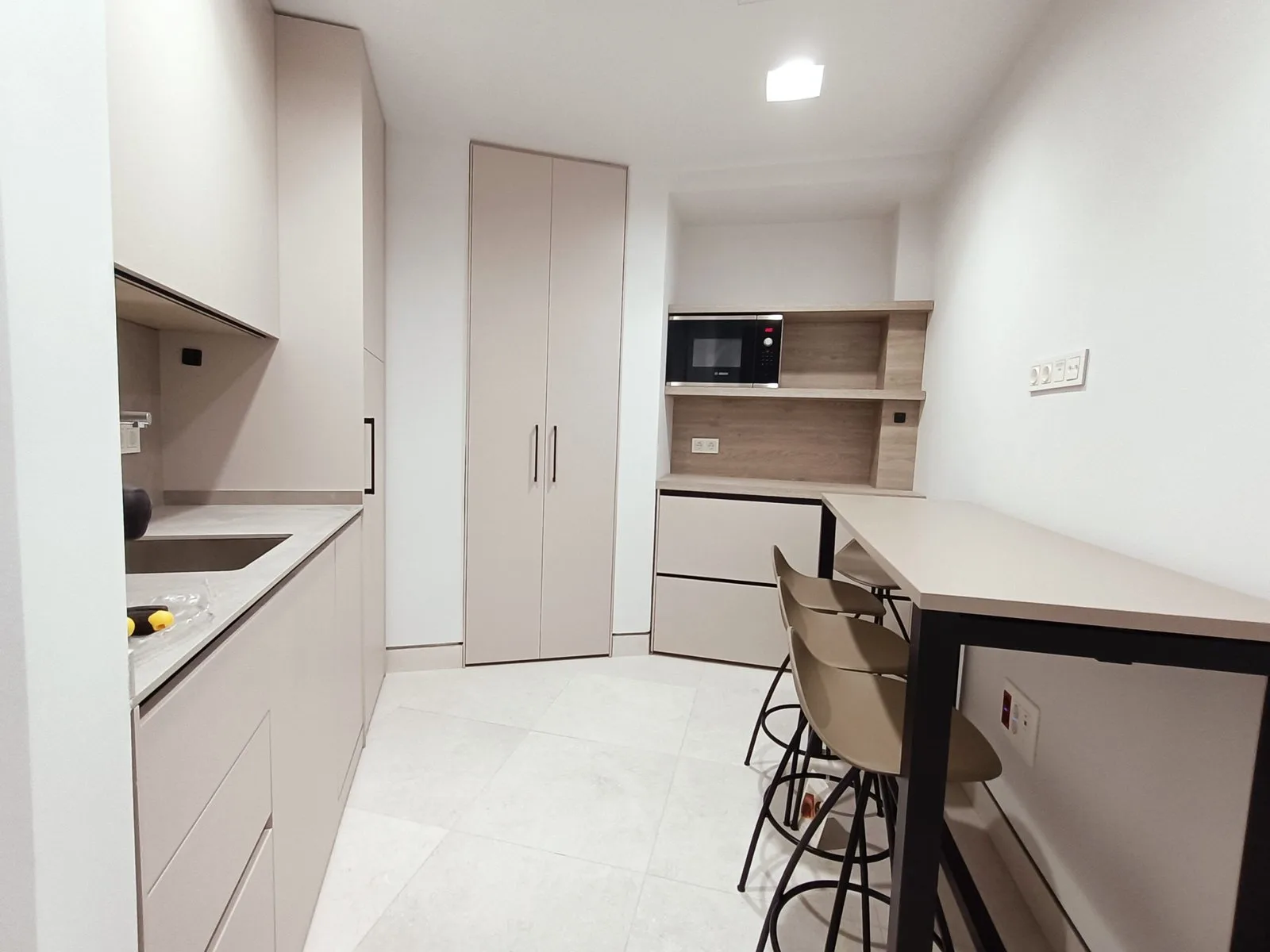 Cocina blanca abierta con barra, taburetes y estantes de madera