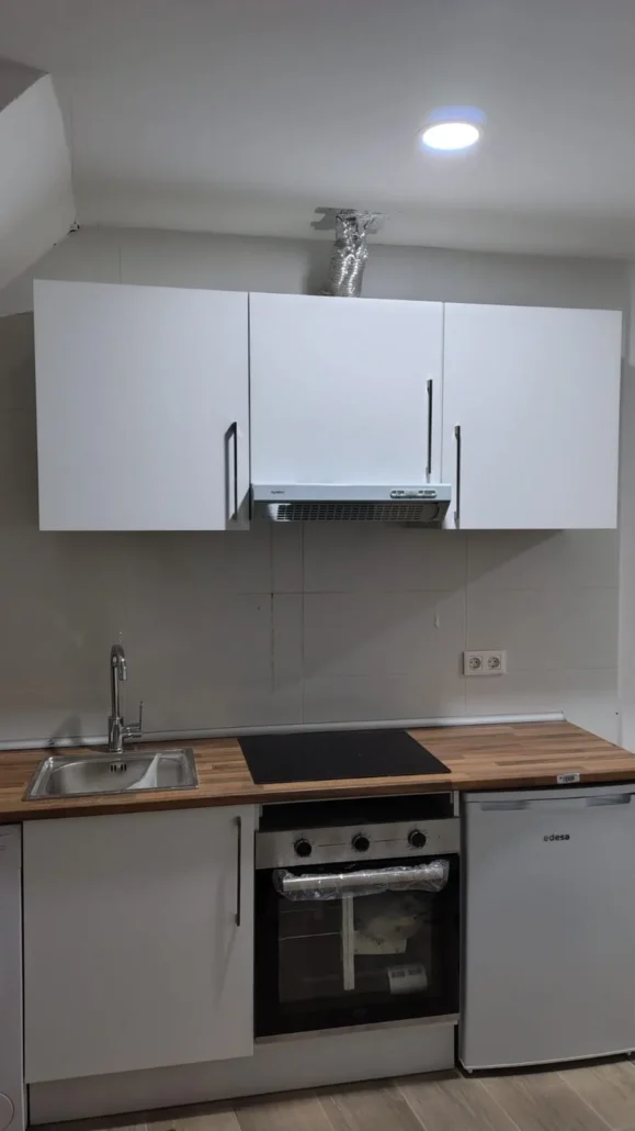 Cocina blanca con encimera de madera, horno y campana montada en Madrid