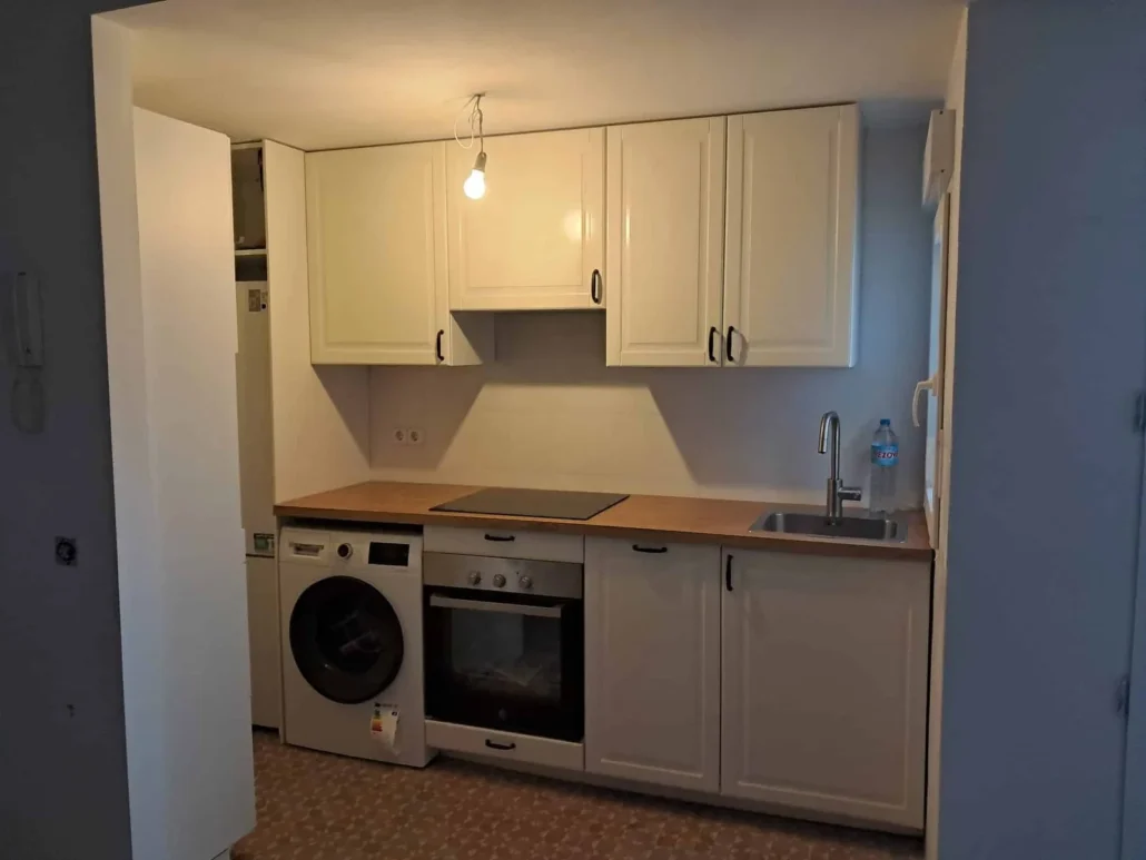 Cocina blanca con encimera de madera y lavadora bajo la encimera