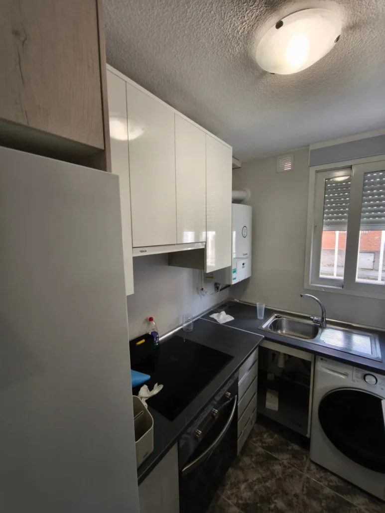 Cocina con muebles claros y encimera negra con lavadora