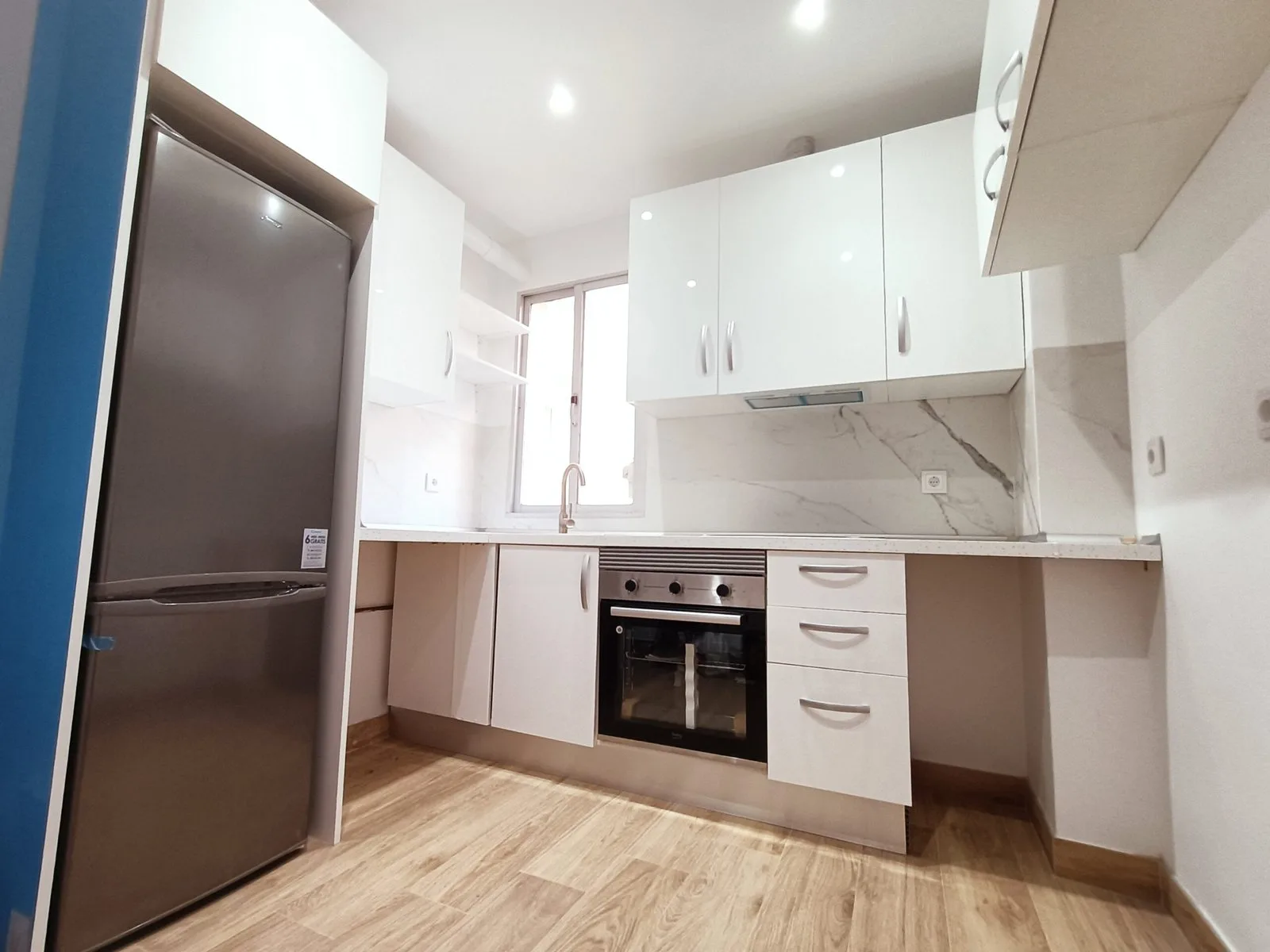 Cocina en L blanca con suelo de madera y nevera de acero