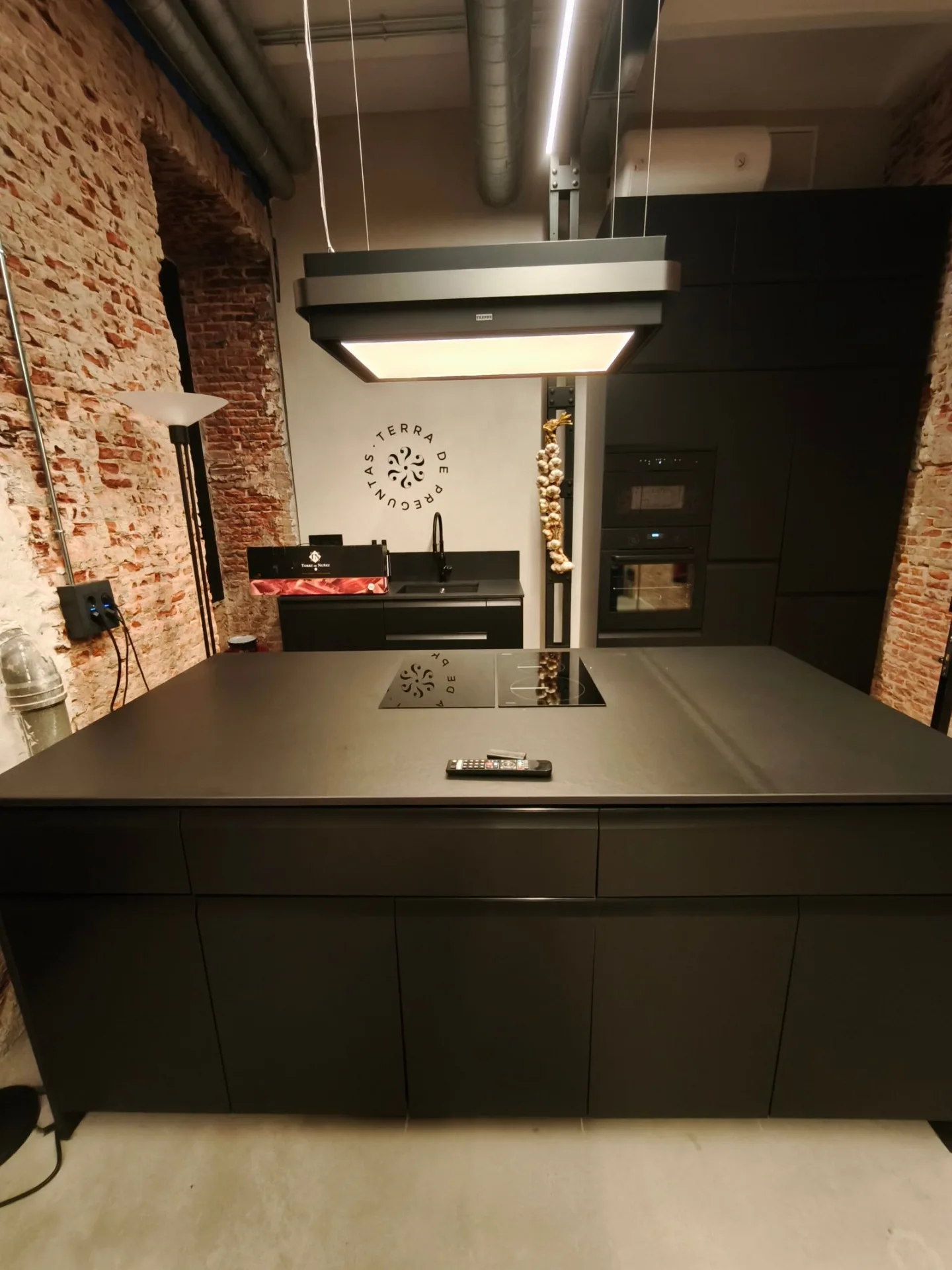 Cocina industrial con isla negra, campana de acero y pared de ladrillo en Madrid