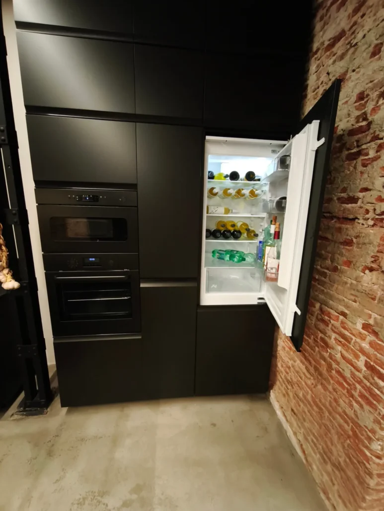 Cocina de muebles negros con nevera integrada y pared de ladrillo